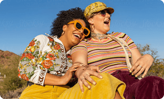 Two women in sunglasses laughing together at sunset outdoors