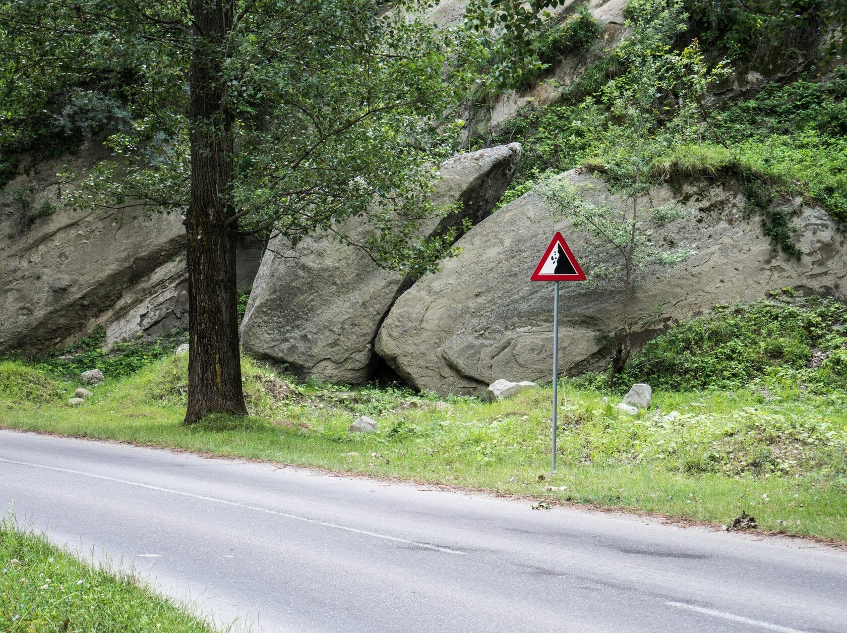 a road side warning of falling rock next to a road in the mountains